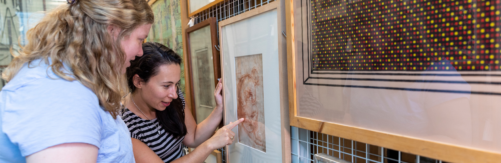 Two women looking at a framed red chalk drawing of a man.