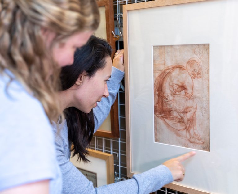 Closeup of two women looking at a framed red chalk drawing of a man.