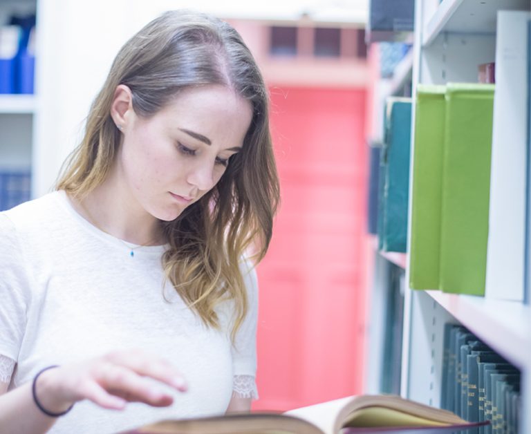 Woman reading a book next to a shelf of books