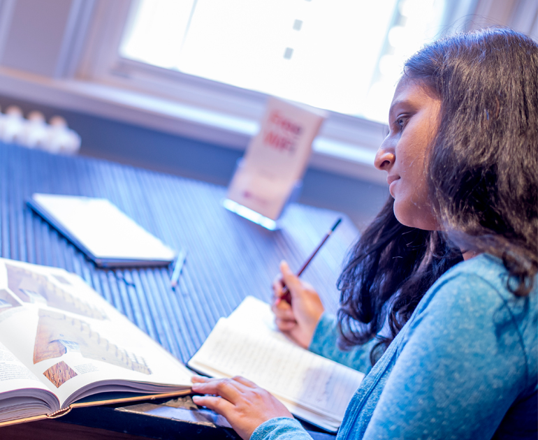 Student writing notes in a notebook and reading a book