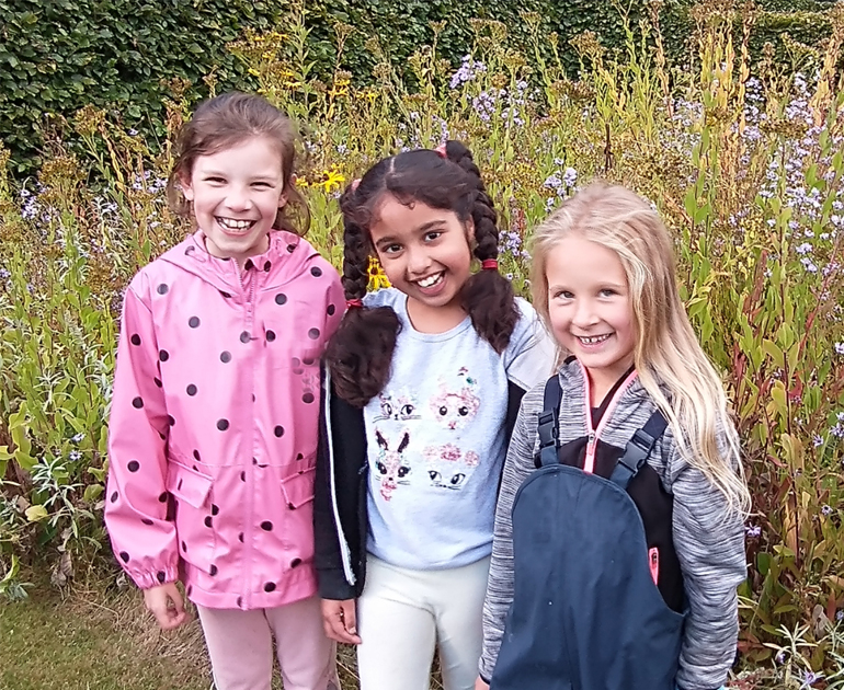 Three girls, smiling, in front of a bed of flowers
