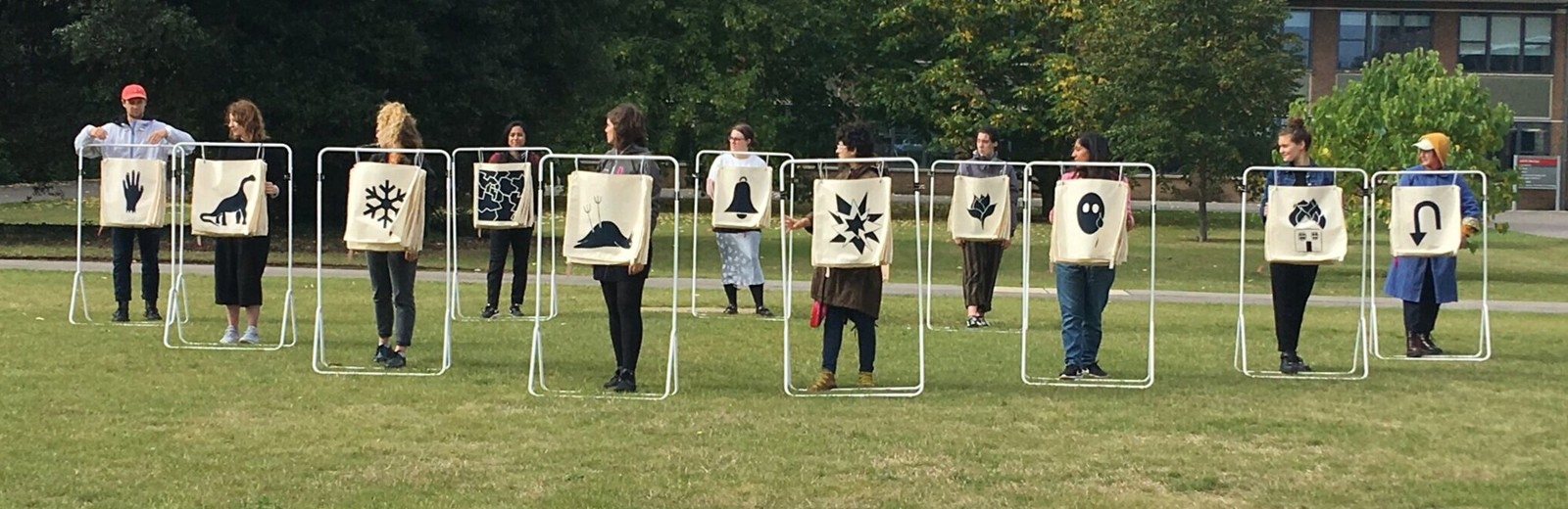 11 figures with metal structures with fabric squares in the centre that appear to work like a flip chart. The figures all have a pictographic image on their square