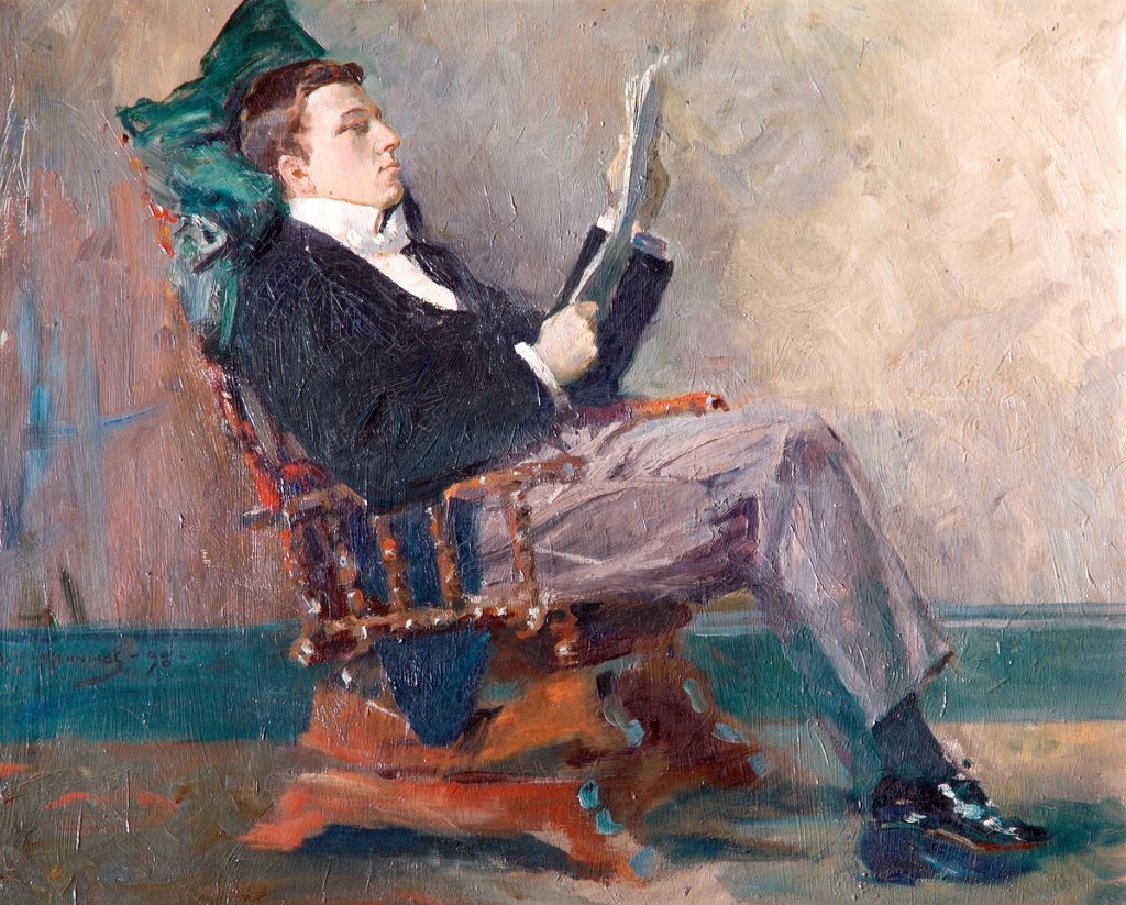 Richard Lloyd Pearson in profile, wearing dinner dress, seated in wooden armchair, legs crossed, reading paper, resting head on green cushion.