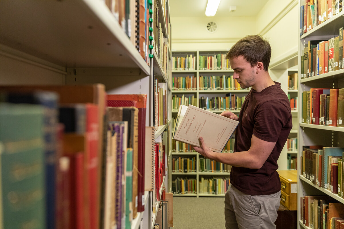 A person reading a large book between shelves in the MERL library