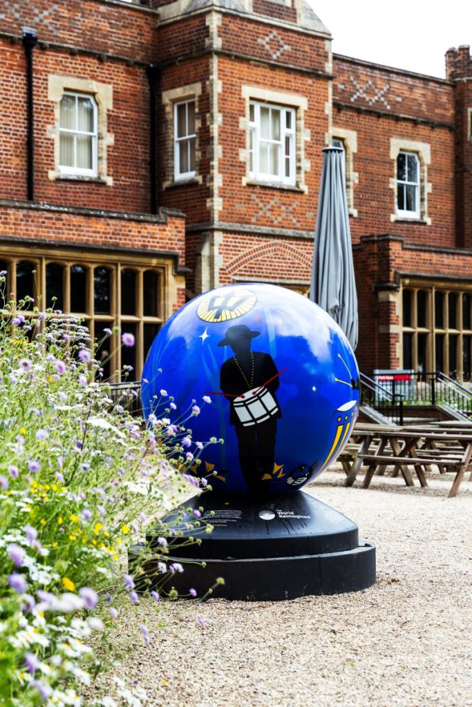 Painted globe with a solid black figure holding a drum, outside Park House (a red brick building).