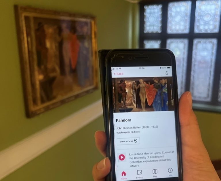 Hand holding a mobile phone open to a digital guide. The page open is for Pandora by John Dickson Batten, which is the artwork in the back of the image