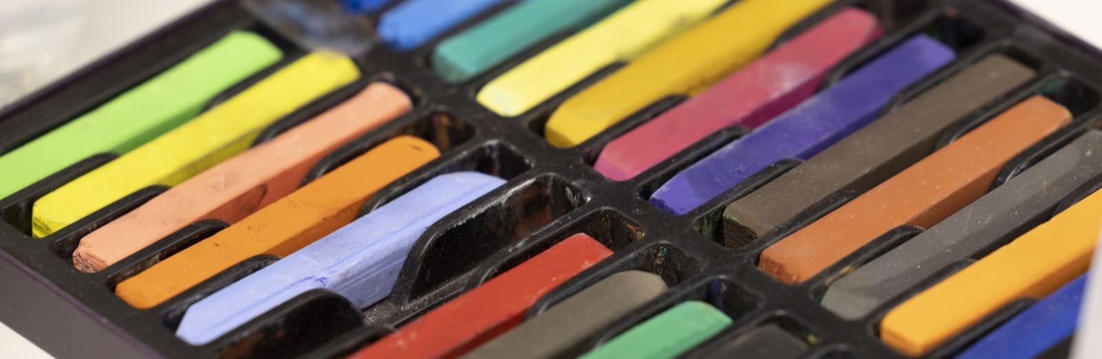 A series of colourful pastel sticks in a black plastic container.