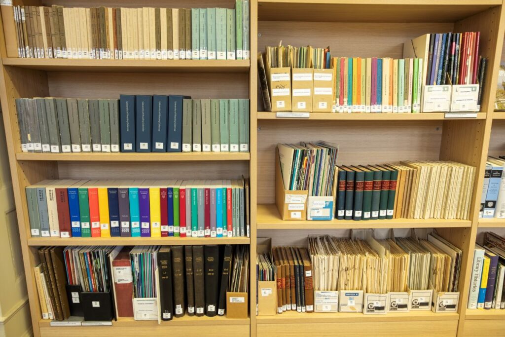 Shelves displaying library items from the University History Collection, including bound volumes and boxed serials.