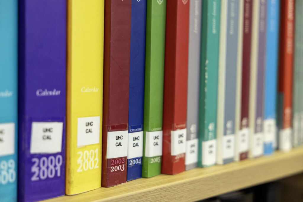 Shelf of University of Reading calendars by year, spines in different colours.