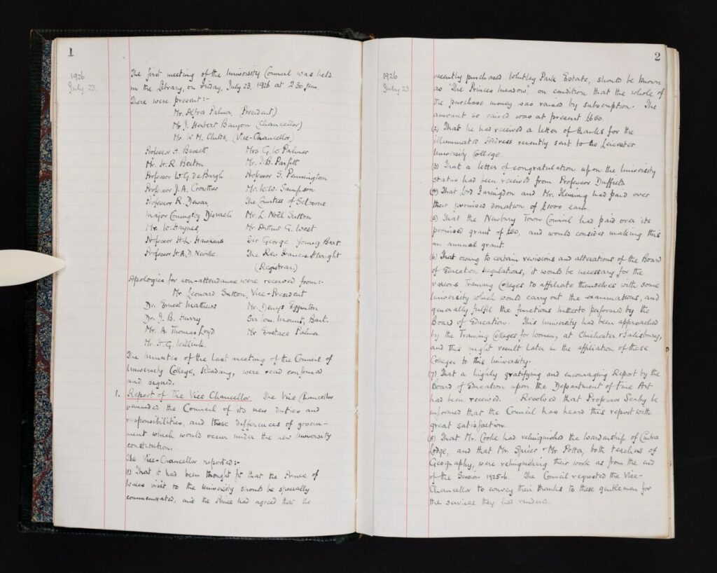 Open ledger showing two facing pages of handwritten council minutes dated July1926. The pages are ruled with red margins and filled with neat pen-written notes listing names, motions, and decisions. Page numbers “1” and “2” appear at the top. The book’s aged paper and cloth-bound spine are visible against a dark background.