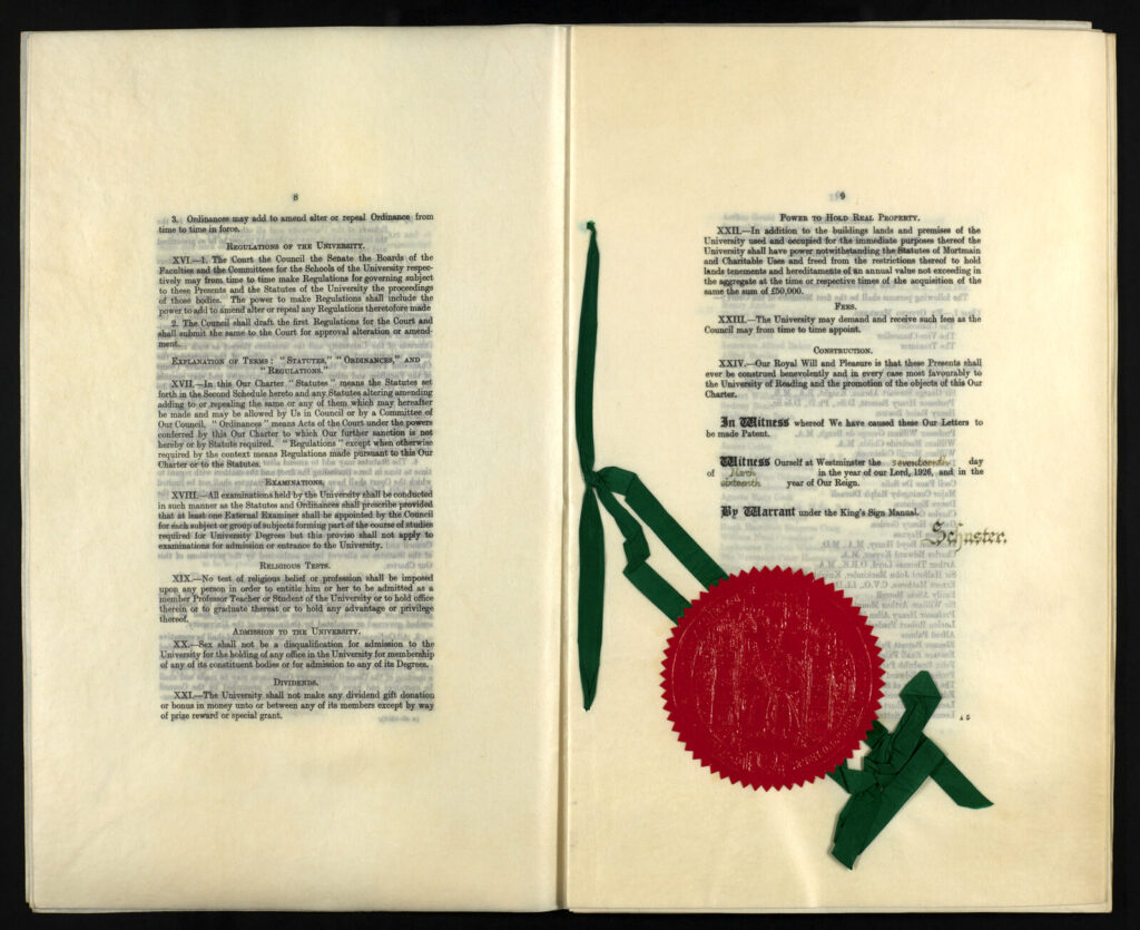 Open charter document with printed text and a large red wax seal attached with green ribbons.