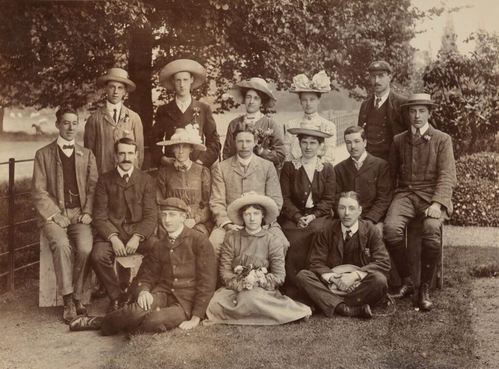 Black and white group photograph of members of University College Reading's Horticultural Department in the College Gardens, arranged in three rows - standing, seated on a bench, and seated on the ground, including F W Keeble (Director) and named staff and students, the women wearing large decorated hats